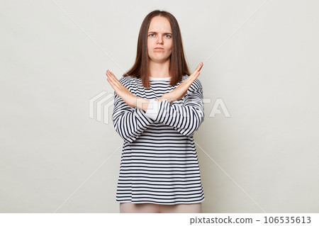 This is the end and no way more. Unhappy woman with brown hair wearing striped casual shirt standing isolated over gray background showing crossed hands. 106535613