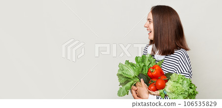 Attractive woman embraces fresh vegetables posing isolated over white background looking away ant advertisement area, copy space for promotional text. Attractive woman embraces fresh vegetables posing isolated over white background looking away ant advertisement area, copy space for promotional text. 106535829