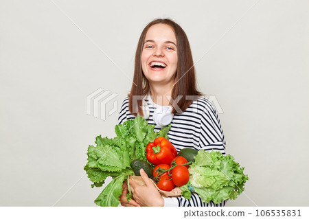Beautiful smiling woman embraces fresh vegetables posing isolated over white background looking at camera with happy face calls on to eat organic food. Beautiful smiling woman embraces fresh vegetables posing isolated over white background looking at camera with happy face calls on to eat organic food. 106535831