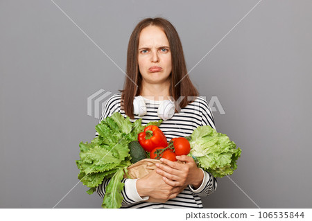 Sad unhappy Caucasian woman holding organic vegetables standing isolated over gray background buying food on market unhappy of high price. Sad unhappy Caucasian woman holding organic vegetables standing isolated over gray background buying food on market unhappy of high price. 106535844