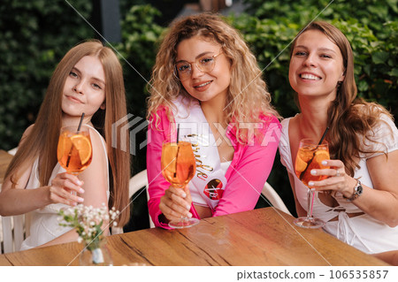 Three girls sits in cafe and drinks cocktails. Happy friends celebrate event together Three girls sits in cafe and drinks cocktails. Happy friends celebrate event together 106535857