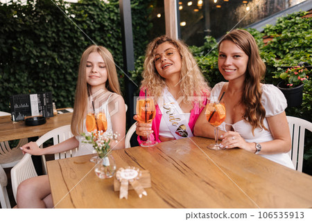 Three girls sits in cafe and drinks cocktails. Happy friends celebrate event together 106535913