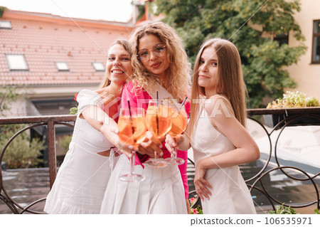 Three female sits by the table and drink orange cocktails. Meet after the years. Hen party. Bride to be  106535971