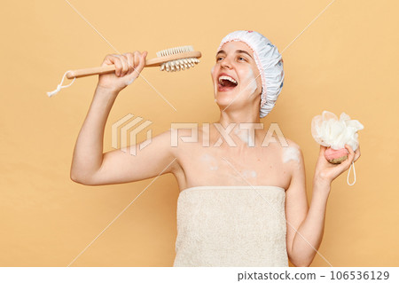 Playful positive woman taking shower in bathroom holding washcloth and body brush for scrub and massage like microphone singing happily having fun while doing skin care procedures. Playful positive woman taking shower in bathroom holding washcloth and body brush for scrub and massage like microphone singing happily having fun while doing skin care procedures. 106536129
