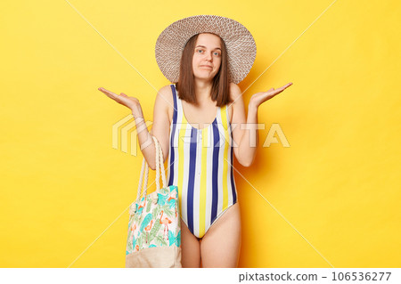 Puzzled uncertain woman wearing swimsuit isolated on yellow background standing with confused expressing shrugging shoulders do not know information about vacation departure. Puzzled uncertain woman wearing swimsuit isolated on yellow background standing with confused expressing shrugging shoulders do not know information about vacation departure. 106536277