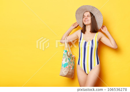 Delighted attractive woman wearing swimsuit isolated on yellow background standing looking away copy space for promotional text advertisement area. Delighted attractive woman wearing swimsuit isolated on yellow background standing looking away copy space for promotional text advertisement area. 106536278
