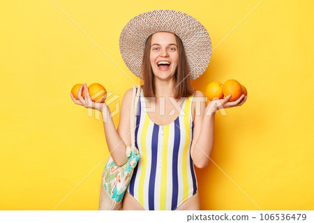 Young caucasian positive woman wearing swimsuit isolated on yellow background showing many oranges smiling happily having excellent holiday in the south. 106536479