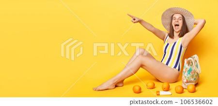 Amazed excited woman wearing striped swimming suit and hat isolated on yellow background pointing far away copy space for promotion advertisement of tropical resort. Amazed excited woman wearing striped swimming suit and hat isolated on yellow background pointing far away copy space for promotion advertisement of tropical resort. 106536602