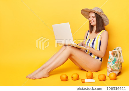 Hard working attractive woman wearing one piece swimming suit posing isolated over yellow background working on resort sitting with laptop enjoying her remote work. Hard working attractive woman wearing one piece swimming suit posing isolated over yellow background working on resort sitting with laptop enjoying her remote work. 106536611
