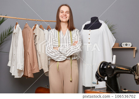 Caucasian self-employed dressmaker woman at workplace work with textile for new fashion clothes collection in her sewing studio, standing with folded hands with confident expression. Caucasian self-employed dressmaker woman at workplace work with textile for new fashion clothes collection in her sewing studio, standing with folded hands with confident expression. 106536702