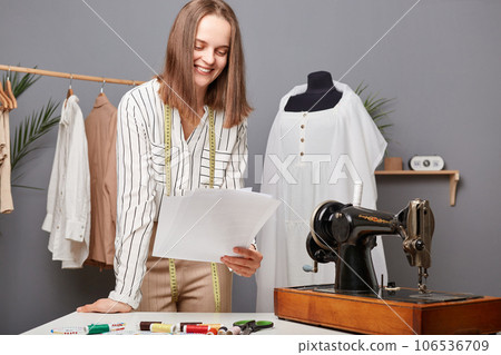 Small garment business owner. Caucasian fashion designer holding papers with sketch in workshop, thinking about new ides for dresses, needlewoman working process. Small garment business owner. Caucasian fashion designer holding papers with sketch in workshop, thinking about new ides for dresses, needlewoman working process. 106536709