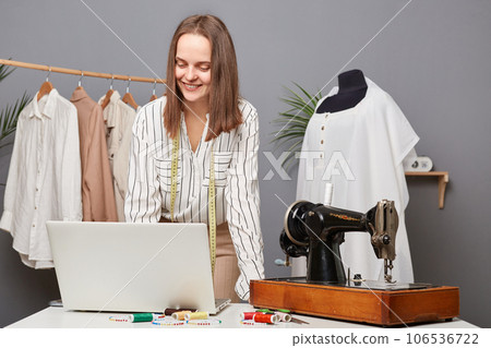 Creative sewing sewer brainstorming new collection working on laptop in tailoring workshop, doing business entrepreneur work on computer, posing in atelier. Creative sewing sewer brainstorming new collection working on laptop in tailoring workshop, doing business entrepreneur work on computer, posing in atelier. 106536722