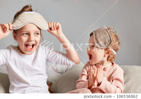 Sisters, with sleeping masks on their eyes, enjoying their time together in the bedroom, laughing and having good time, waking up in good mood and spend their leisure time on the weekend. 106536862