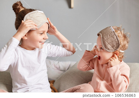 Happy kids sisters spending time together in bedroom, wearing blindfolds on their eyes, laughing and having fun, feeling refreshed and happy, spending their leisure time on the weekend morning. Happy kids sisters spending time together in bedroom, wearing blindfolds on their eyes, laughing and having fun, feeling refreshed and happy, spending their leisure time on the weekend morning. 106536863