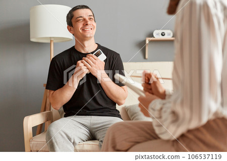 Satisfied delighted smiling man in casual T-shirt sitting at psychologist office and talking with specialist enjoying therapy session, having grateful expression. 106537119
