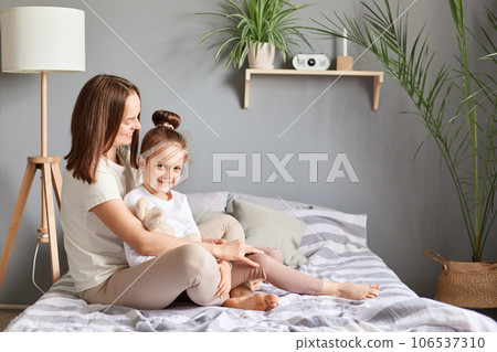 Profile portrait of mother embracing daughter in bedroom at home sitting together hugging home leisure positive emotions parenthood love. 106537310