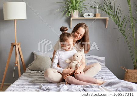 Mother's day. Caucasian mother and daughter sitting in bed woman hugging her cute child smiling and expressing positive emotions family time. Mother's day. Caucasian mother and daughter sitting in bed woman hugging her cute child smiling and expressing positive emotions family time. 106537311