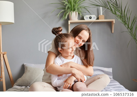 Young girl sitting with her mother in their cozy room, smiling and feeling togetherness of relationship, enjoying leisurely day filled with love and relaxation. 106537316