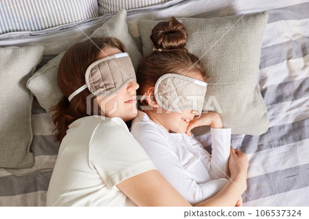 Little girl and her mother enjoying morning sleeping together hugging wearing blindfolds having day napping together in bedroom lazy weekend. Little girl and her mother enjoying morning sleeping together hugging wearing blindfolds having day napping together in bedroom lazy weekend. 106537324