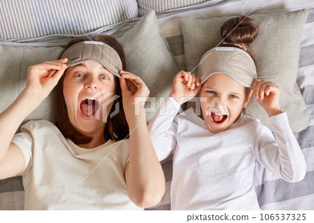 Good time at home. Playful joyful girl and her mother enjoying sunny morning, child and mom wake up from sleep playing on bed in bedroom raised blindfolds screaming with happiness. Good time at home. Playful joyful girl and her mother enjoying sunny morning, child and mom wake up from sleep playing on bed in bedroom raised blindfolds screaming with happiness. 106537325