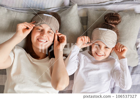 Mother and daughter enjoyed lazy morning together in cozy bedroom, wake up slowly, taking off blindfolds looking at camera smiling expressing positive emotions. Mother and daughter enjoyed lazy morning together in cozy bedroom, wake up slowly, taking off blindfolds looking at camera smiling expressing positive emotions. 106537327