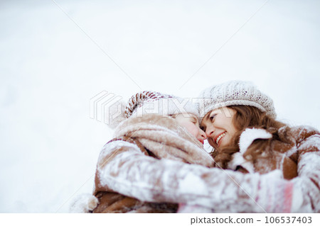 smiling stylish mother and daughter laying in snow 106537403