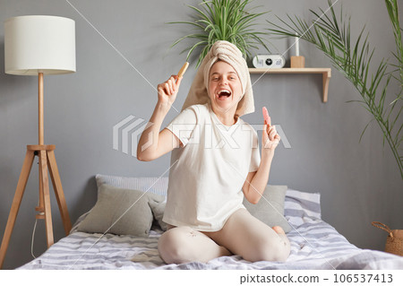 Cheerful happy overjoyed woman in white towel holding new sponges for beauty procedures dancing in bed in morning after shower playful weekend time. Cheerful happy overjoyed woman in white towel holding new sponges for beauty procedures dancing in bed in morning after shower playful weekend time. 106537413