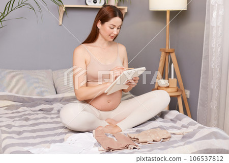 Pregnant woman getting ready for the maternity hospital, packing baby stuff, female with bare belly preparing and planning baby clothes. List of things in the hospital. 106537812