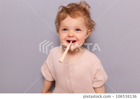 Positive laughing little child baby brushing teeth isolated over gray background holding toothbrush in mouth smiling having fun while doing dental care procedures, oral hygiene. 106538136