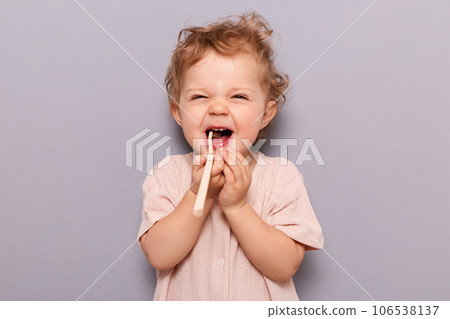 Oral hygiene. Dental care. Laughing funny little child baby brushing teeth isolated over gray background enjoying wearing t-shirt, free space for advertisement. 106538137