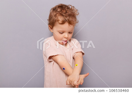 Cute funny little caucasian girl infant posing isolated over gray background showing tongue out looking at her hands with colorful stickers having fun. Cute funny little caucasian girl infant posing isolated over gray background showing tongue out looking at her hands with colorful stickers having fun. 106538460