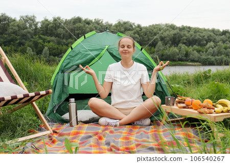 Relaxed calm woman with bun hairstyle sitting with crossed legs in lotus pose meditating practicing yoga in open air, being satisfied and delighted. Relaxed calm woman with bun hairstyle sitting with crossed legs in lotus pose meditating practicing yoga in open air, being satisfied and delighted. 106540267