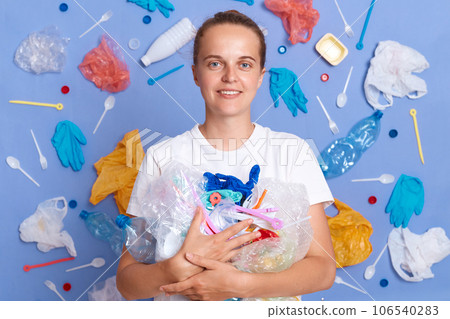 Eco-friendly environment protection. Displeased serious woman volunteer wearing white shirt isolated on blue wall with rubbish around cleaning up rubbish. 106540283