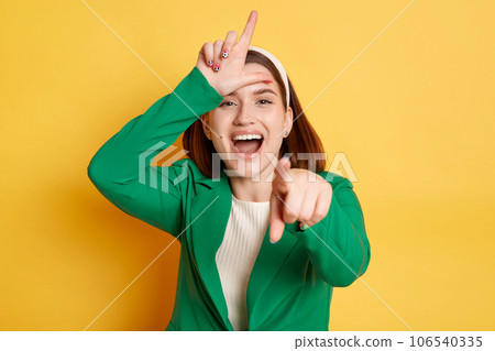 Funny laughing woman wearing green jacket posing isolated over yellow background showing looser gesture pointing at you expressing positive emotions. Funny laughing woman wearing green jacket posing isolated over yellow background showing looser gesture pointing at you expressing positive emotions. 106540335