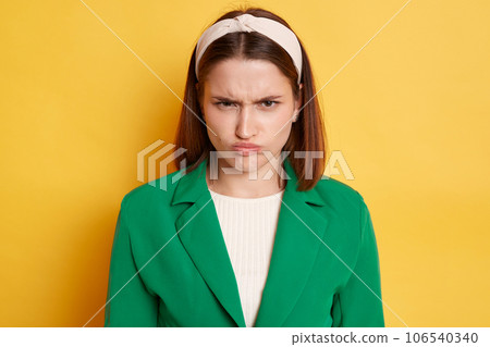 Offended unhappy angry woman wearing green jacket posing isolated over yellow background looking at camera frowning face offended negative feelings. Offended unhappy angry woman wearing green jacket posing isolated over yellow background looking at camera frowning face offended negative feelings. 106540340
