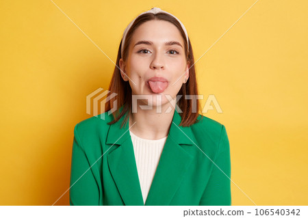 Positive cute woman wearing green jacket posing isolated over yellow background showing tongue out having fun disobedient behavior. 106540342