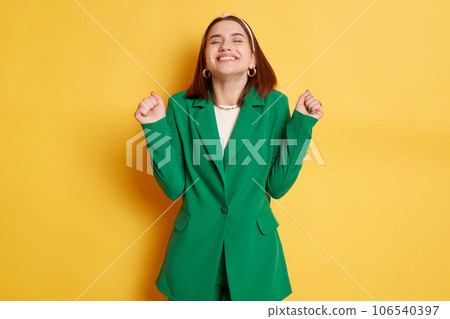 Extremely happy woman wearing green jacket standing isolated over yellow background closed her eyes clenched fists celebrating her success. 106540397