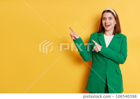 Amazed woman wearing green jacket standing isolated over yellow background presenting empty space pointing with fingers mockup advertisement area. Amazed woman wearing green jacket standing isolated over yellow background presenting empty space pointing with fingers mockup advertisement area. 106540398
