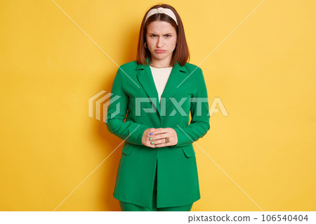 Sad unhappy woman wearing green jacket standing isolated over yellow background standing with pout lips being offended expressing negative emotions. 106540404