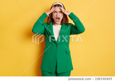 Despair shocked sad woman wearing green jacket standing isolated over yellow background screaming with negative emotions being depressed. 106540405