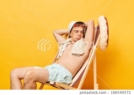 Confused shirtless man sitting on deck chair isolated over yellow background raised his arms smelling unpleasant disgust sweat odor. 106540572