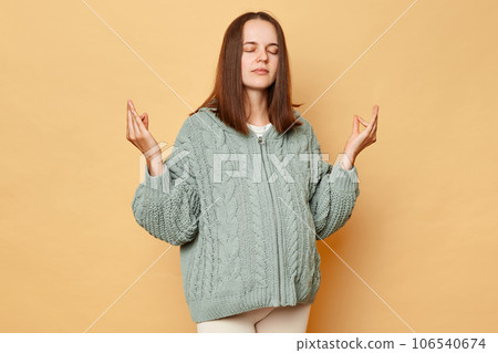 Calm young pregnant woman wearing knitted sweater standing isolated over beige background posing with closed eyes practicing yoga trying to relax. 106540674
