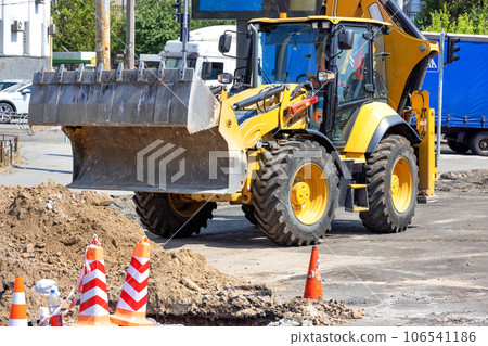 Construction tractor with a hydraulic sliding bucket on a repaired section of the road on a sunny day. 106541186