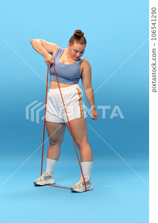 Young overweight plus size woman wears top warm up training use elastic band band for hands isolated on blue background studio. Workout sport concept 106541290