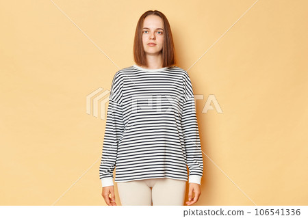 Serious strict brown haired woman wearing striped shirt standing isolated over beige background looking nat camera with bossy stressed expression, being in bad mood. Serious strict brown haired woman wearing striped shirt standing isolated over beige background looking nat camera with bossy stressed expression, being in bad mood. 106541336