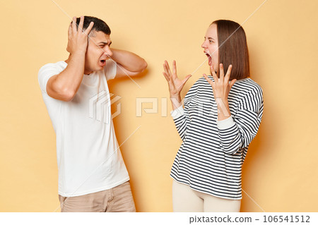 Irritated frustrated young couple wife and husband wearing casual attires arguing screaming having conflict standing isolated over beige background 106541512
