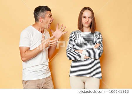 Crazy mad young man screaming with aggression arguing with brown haired woman in casual clothing standing isolated over beige background, having relationship problems. Crazy mad young man screaming with aggression arguing with brown haired woman in casual clothing standing isolated over beige background, having relationship problems. 106541513