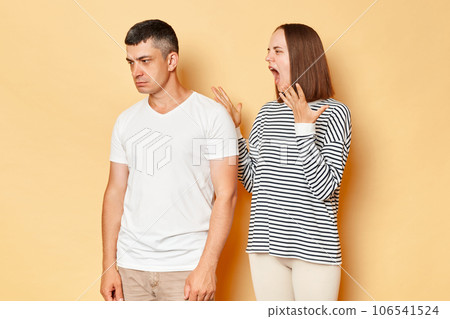 Mad crazy young wife screaming to husband wearing casual attires standing isolated over beige background family conflict relationship problems. Mad crazy young wife screaming to husband wearing casual attires standing isolated over beige background family conflict relationship problems. 106541524