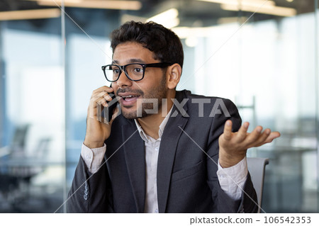 Dissatisfied and upset man talking on phone close up, businessman young in business clothes at workplace inside office. 106542353