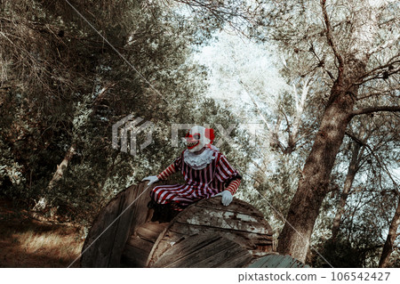 evil clown perched on a cable reel in the woods evil clown perched on a cable reel in the woods 106542427